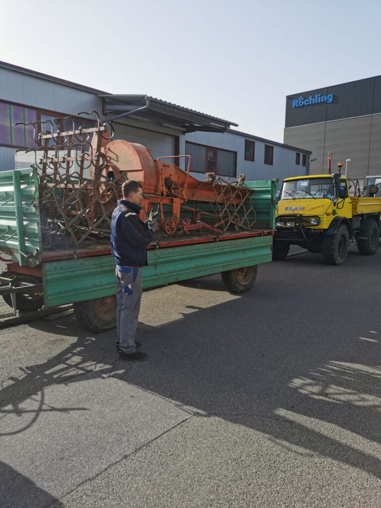 Bild, welches das Abladen von alten Landwirtschaftsgeräten aus Metall zeigt