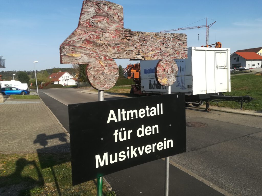 Bild, welches ein Schild mit einem Unimog aus Holz und der Schrift "Altmetall für den Musikverein" zeigt